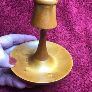 以下が含まれることがあります： 小さな丸い土台と背の高い細い茎を持つ木製リングホルダー。ホルダーは薄い茶色の木でできており、滑らかで磨かれた仕上げになっています。