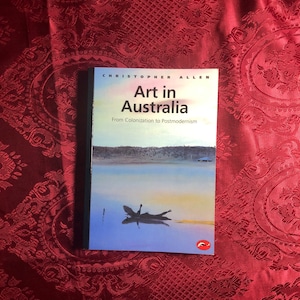 May include: A book titled "Art in Australia: From Colonization to Postmodernism" by Christopher Allen. The cover features a photograph of a body of water with a log floating on the surface.