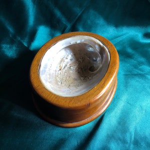 May include: A wooden bowl with a mother-of-pearl inlay. The bowl is round and has a smooth, polished finish.