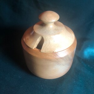 May include: A wooden sugar bowl with a lid. The bowl is light brown and has a smooth, rounded shape. The lid has a small knob on top.