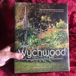 May include: A book titled "Wychwood" with a garden scene on the cover. The cover features a garden with a decorative structure and text that reads "The most beautiful garden in Tasmania" and "The making of one of the world's most magical gardens."