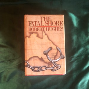 May include: The cover of a paperback book titled "The Fatal Shore" by Robert Hughes. The cover features a map of Australia with a chain and shackles.