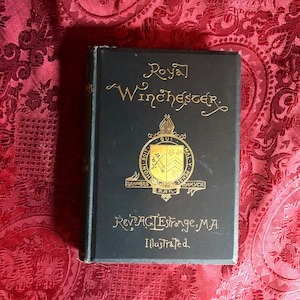May include: A black book with gold lettering titled "Royal Winchester" by Rev AGLEstrange, MA. The book is illustrated and features a coat of arms on the cover.