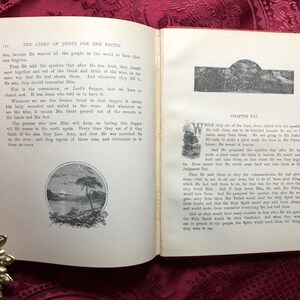 May include: An open book with a red cover and white pages. The book is titled "The Story of Jesus for the Young." The pages contain text and illustrations. The book is open to a page with the title "Chapter XXI." The text on the page describes Jesus talking to his apostles.
