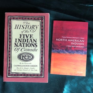 May include: Two books about North American history. The book on the left is titled "The History of the Five Indian Nations of Canada 1747" by Cadwallader Colden. The book on the right is titled "North American Indians: A Very Short Introduction" by Theda Perdue and Michael D. Green. Both books have red covers.