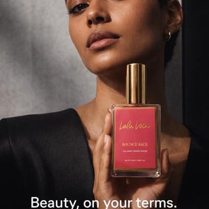 May include: A woman holds a clear glass bottle of Lala Lova Bounce Back Collagen Firming Serum. The bottle has a gold cap and a red label with gold lettering. The text "Beauty, on your terms" is below the bottle.