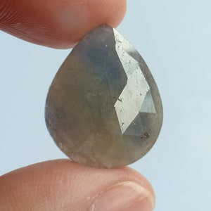 Pode incluir: Uma gema facetada em forma de pêra com uma cor cinza e azul.