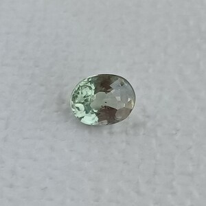 May include: A light green oval-shaped gemstone with a slight brown hue.
