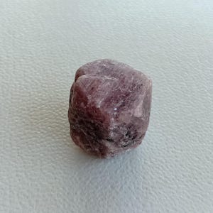 May include: A rough, pink ruby crystal with a natural, faceted shape.