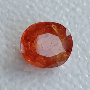 May include: A vibrant orange oval-shaped gemstone with a faceted cut. The gemstone has a translucent appearance with a slight golden hue.
