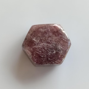 May include: A hexagonal, faceted, pink ruby crystal with a rough, natural texture.