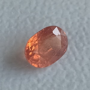 May include: A light orange oval-shaped gemstone with a faceted cut.