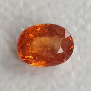 May include: A vibrant orange oval-shaped gemstone with a smooth, polished surface.