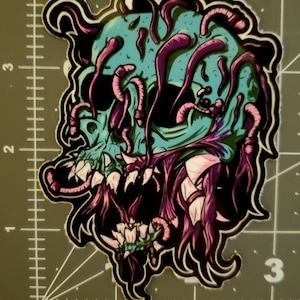May include: A sticker featuring a skull with purple and pink tentacles growing out of its head and mouth. The skull is green and has a black outline.