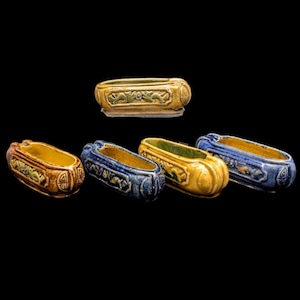 May include: A set of five elongated ceramic brush rests featuring a hollow center and raised relief carvings of dragons on the sides. The pieces are finished in glossy glazes of mustard yellow, deep blue, and brown, with a smooth interior surface.