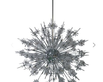 May include: A large, modern chandelier with a chrome finish and a starburst design. The chandelier is made up of many small, crystal-like pieces that are arranged in a radial pattern. The chandelier is suspended from a single, thin chain.