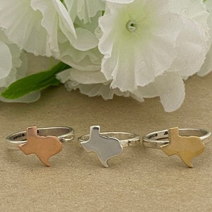 May include: Three silver rings with a Texas state outline design. The rings are in three different finishes: silver, gold, and copper.