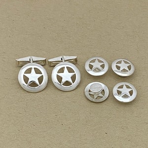 May include: A set of silver cufflinks and shirt studs featuring a five-pointed star design. The cufflinks have a silver bar to connect the two pieces.