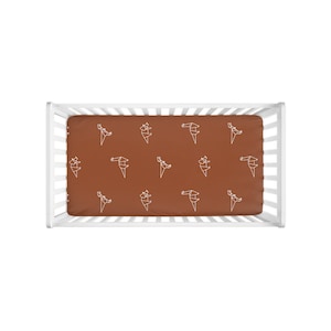 May include: A white crib with a brown fitted sheet featuring a white geometric pattern. The sheet has a repeating pattern of origami-style birds.