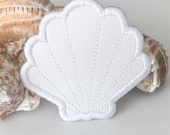 May include: A white seashell-shaped embroidered patch with a white border and stitched details. The patch is placed next to a natural seashell with brown and tan patterns, suggesting a beach or nautical theme.
