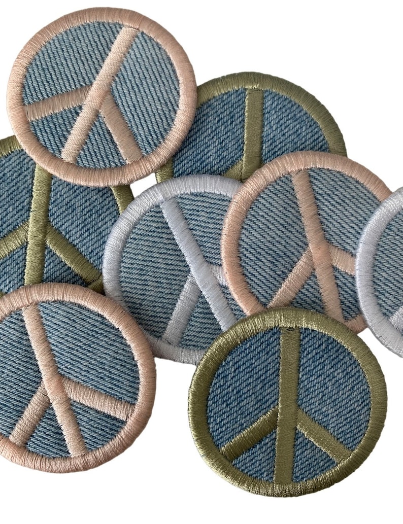 May include: A collection of denim peace sign patches with different colored stitching. The patches are round and have a light blue denim background with a white peace sign in the center. The stitching around the peace sign is in various colors, including pink, green, and white.