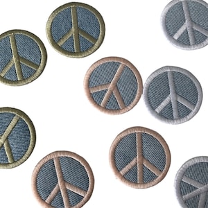 May include: Nine embroidered peace sign patches in various colors. The patches are circular and feature a white peace sign on a denim background. The patches are surrounded by a contrasting colored border.