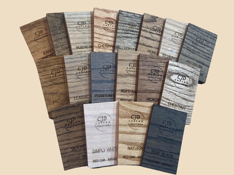 A collection of stained wood sample swatches arranged in a fan layout, each labeled with the stain color and wood type. Swatches include shades like Sedona, Cherry, Dark Walnut, Ebony, Slate, Red Mahogany, and Golden Oak, all engraved with the "CJD Custom Creations" logo. These samples show how different Minwax stains appear on Red Oak wood, helping customers choose the right finish for their woodworking or home improvement projects.