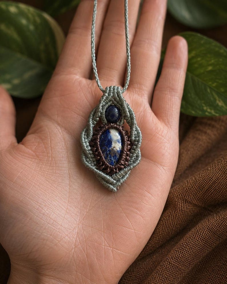 May include: A handmade macrame pendant necklace featuring a central oval blue stone with white inclusions, surrounded by a woven design in shades of blue and brown. The necklace has a light blue cord.
