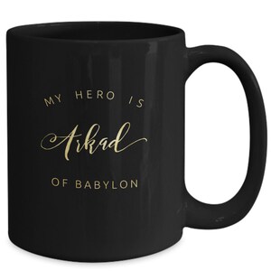 May include: Black ceramic coffee mug with a gold inscription that reads "My hero is Arkad of Babylon".