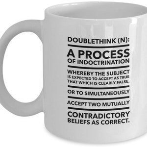 May include: White ceramic coffee mug with black text that reads "DOUBLETHINK (N): A PROCESS OF INDOCTRINATION WHEREBY THE SUBJECT IS EXPECTED TO ACCEPT AS TRUE THAT WHICH IS CLEARLY FALSE, OR TO SIMULTANEOUSLY ACCEPT TWO MUTUALLY CONTRADICTORY BELIEFS AS CORRECT."