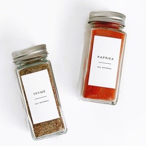 two glass spice jars with a white label with black writing with a minimalist and modern clean font. waterproof labels with text reading the spice, a line and all natural in smaller text on the bottom.