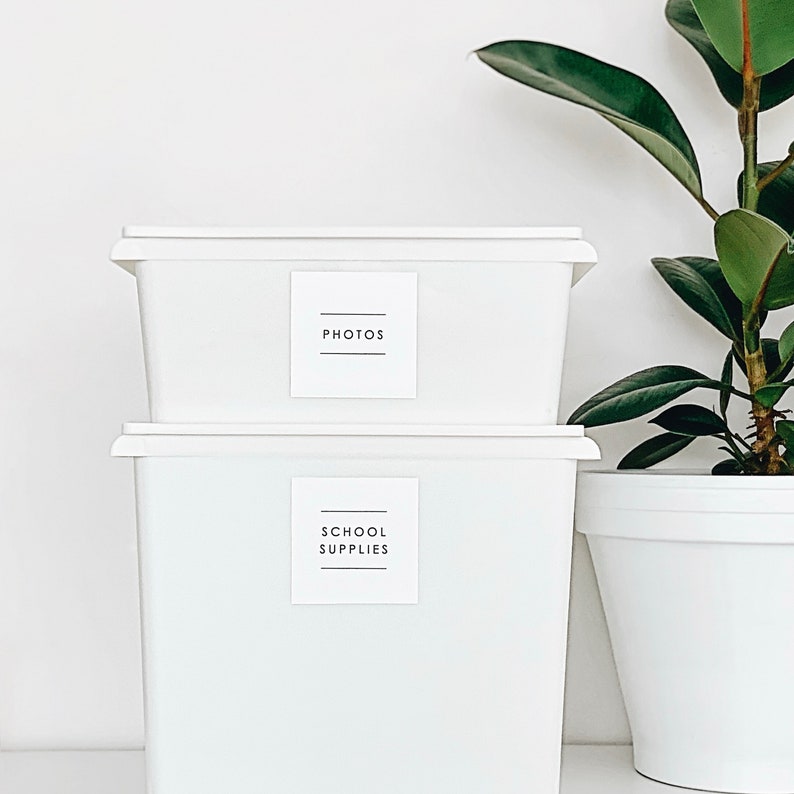 May include: Two white plastic storage bins with labels. The top bin is labelled "PHOTOS" and the bottom bin is labelled "SCHOOL SUPPLIES".