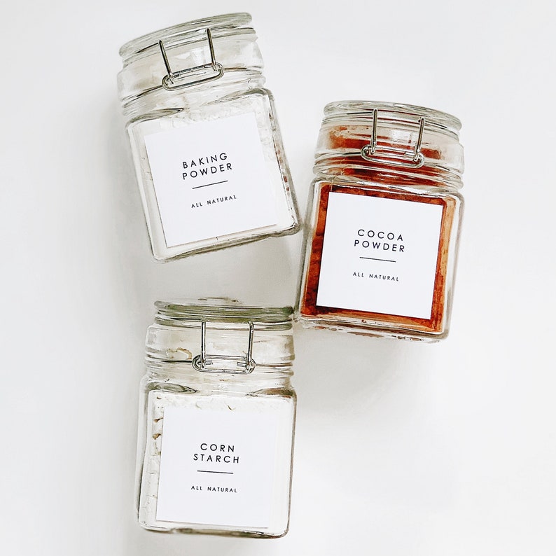 May include: Three glass jars with white labels and black text. The labels read "Baking Powder", "Cocoa Powder", and "Corn Starch". All labels say "All Natural".