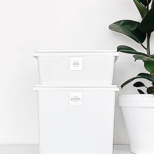 May include: Two white plastic storage bins with labels. The top bin is labelled "Summer Clothes" and the bottom bin is labelled "Halloween Decorations".