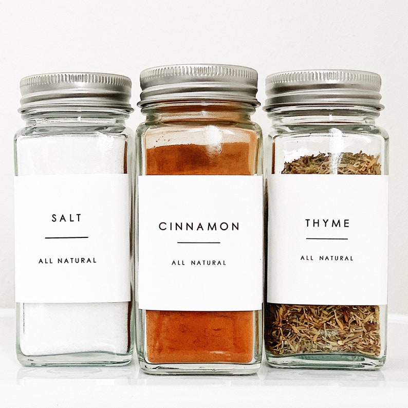 May include: Three glass spice jars with silver lids and white labels. The labels have black text that reads "Salt, All Natural", "Cinnamon, All Natural", and "Thyme, All Natural".