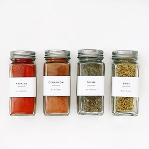 May include: Four glass spice jars with silver lids and white labels. The labels read "Paprika", "Cinnamon", "Thyme", and "Sage". All labels have the text "All Natural" underneath the spice name.