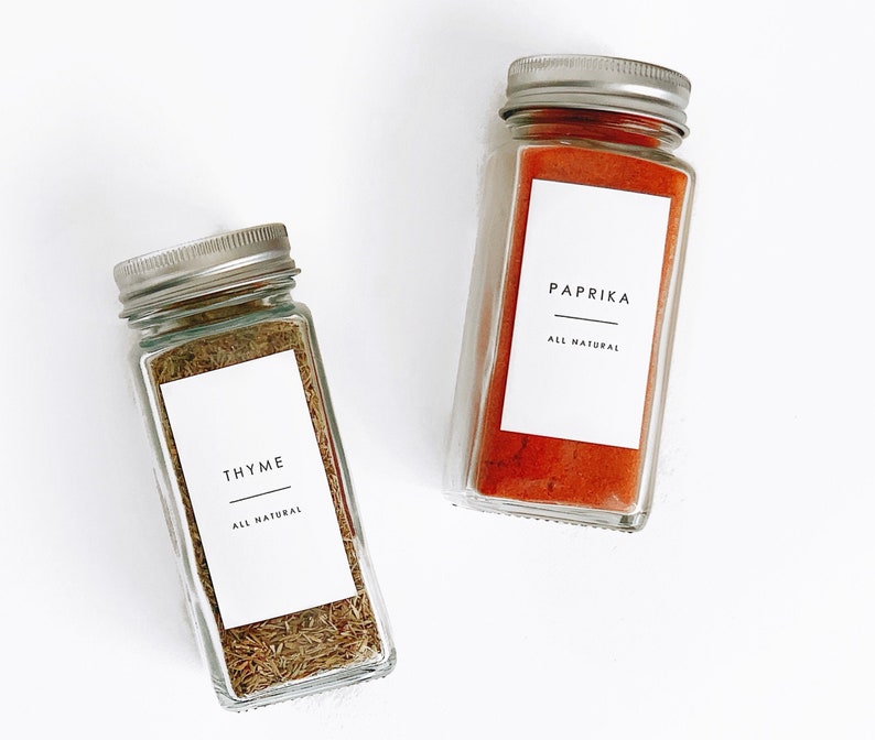 two glass spice jars with a white label with black writing with a minimalist and modern clean font. waterproof labels with text reading the spice, a line and all natural in smaller text on the bottom.