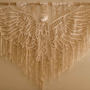 Macrame eagle wall hanging hangs in cotton on a wooden tasmanian oak dowel on a white wall in the evening.