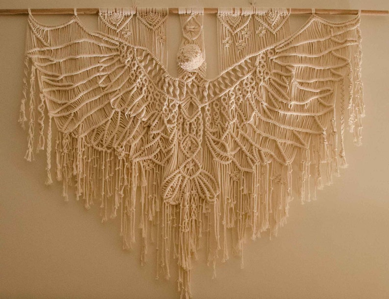 Macrame eagle wall hanging hangs in cotton on a wooden tasmanian oak dowel on a white wall in the evening.