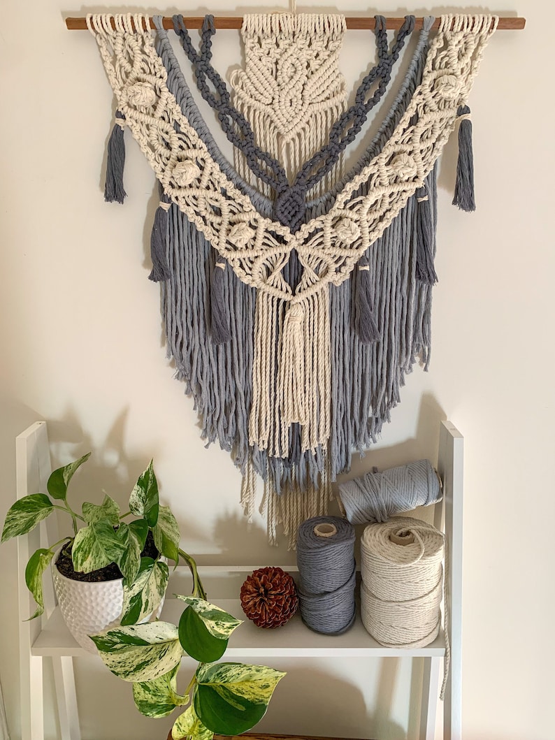 Multicoloured macrame wall hanging pattern with 4 layers and 7 tassels. This is a popular macrame pattern design in shop. Pictured above a potted marble queen plant and stacked macrame cord.