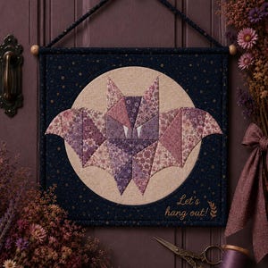 Può includere: Un arazzo quadrato in tessuto con un design a pipistrello in patchwork nei toni del viola e del rosa su uno sfondo circolare beige. Il bordo in tessuto blu scuro presenta un motivo a stelle dorate e il testo ricamato Let's hang out! in oro.