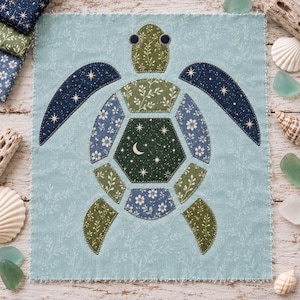 May include: A fabric square featuring a sea turtle appliqué made from various patterned patches. The turtle has a dark green central shell with a crescent moon and stars, surrounded by blue and green floral and celestial fabric pieces.