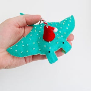 Può includere: Un ornamento a forma di manta raia in feltro turchese con perline bianche e un cappello di Babbo Natale rosso.