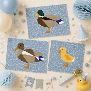 Puede incluir: Tres paneles rectangulares de tela con diseños geométricos de patos sobre un fondo floral azul. Un panel muestra un ánade real macho con cabeza verde, otro una pata marrón y el tercero un pequeño patito amarillo con patas naranjas.