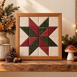 May include: A square fabric wall art piece featuring a geometric star pattern in red, dark green, and cream, encased in a light wood frame. The star design is composed of triangular fabric segments with plaid and solid textures.