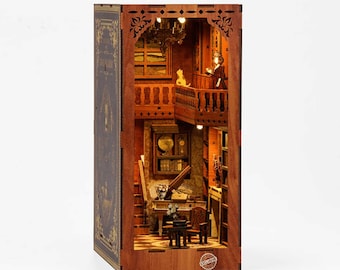 Pode incluir: Uma caixa de madeira em forma de livro com uma cena interior em miniatura. A cena apresenta uma escada, um piano, uma estante de livros e uma figura em pé em uma varanda. A caixa é iluminada por dentro, criando um brilho quente.