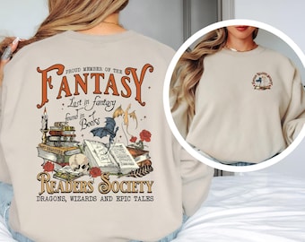 Op de afbeelding: Beige sweatshirt met een afbeelding op de rug met de tekst "Proud Member of the Fantasy Readers Society" met illustraties van boeken, een schedel en een draak. De voorkant heeft een kleinere bijpassende afbeelding.