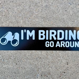 Op de afbeelding: Zwarte en witte sticker met een verrekijker en de tekst "I'M BIRDING GO AROUND".