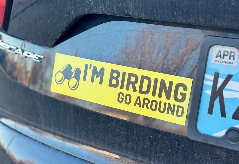 Op de afbeelding: Een gele bumper sticker met zwarte tekst die "I'm Birding Go Around" luidt. Links van de tekst is een verrekijker afgebeeld.