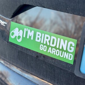 Op de afbeelding: Groene en witte auto sticker met een verrekijker en de tekst "I'm Birding Go Around".